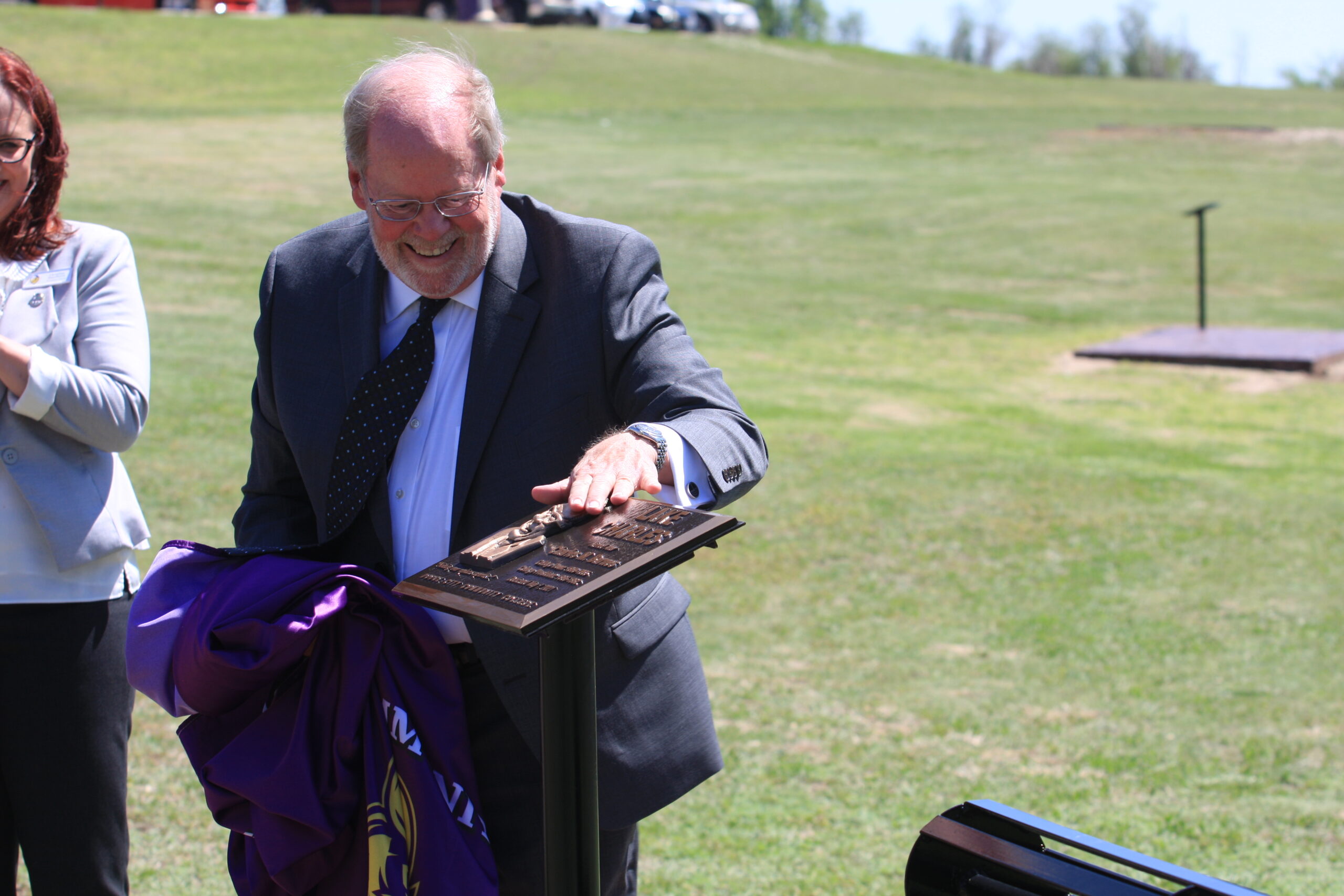 Dr. Roger Barnes unveils the bronze plaque honoring his father, Charles M. Barnes, at the dedication event for DC3’s Lake Charles on May 7. [Photo by Justin Wilson]